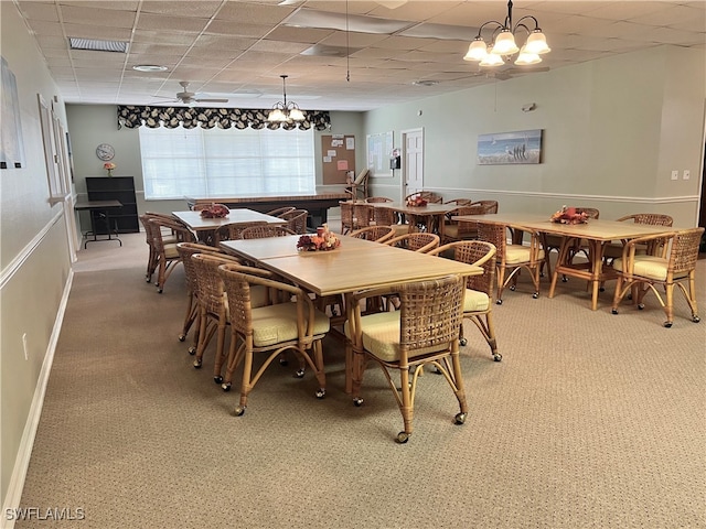 carpeted dining space featuring a drop ceiling and ceiling fan with notable chandelier