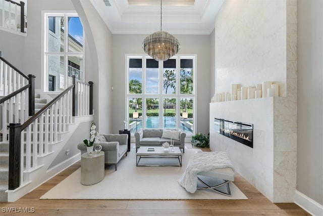 living room with a fireplace, a high ceiling, ornamental molding, a chandelier, and hardwood / wood-style flooring