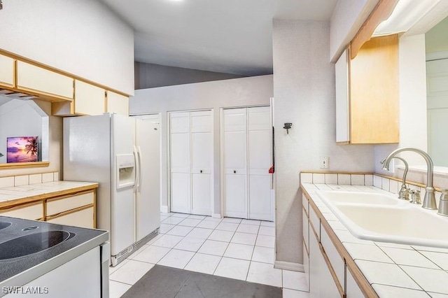 kitchen with light tile patterned floors, vaulted ceiling, tile countertops, sink, and range