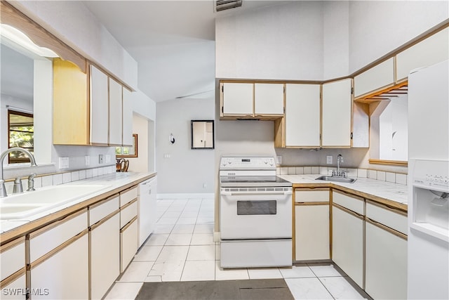 kitchen with lofted ceiling, white appliances, light tile patterned flooring, and sink