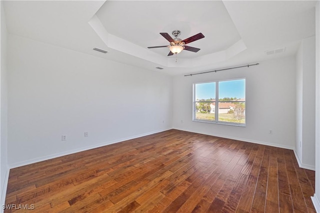 spare room featuring a raised ceiling, ceiling fan, and dark wood-type flooring