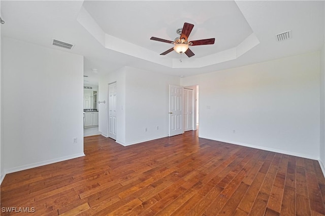 unfurnished room with dark hardwood / wood-style flooring, a tray ceiling, and ceiling fan