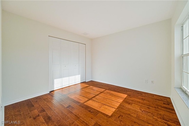 unfurnished bedroom featuring hardwood / wood-style floors, a closet, and multiple windows