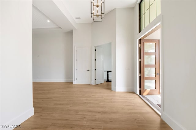 hall with a notable chandelier, a healthy amount of sunlight, light wood-type flooring, and a high ceiling