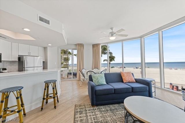 living room featuring a beach view, a water view, light hardwood / wood-style flooring, and ceiling fan