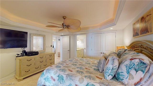 bedroom with ensuite bath, ornamental molding, ceiling fan, a tray ceiling, and a closet