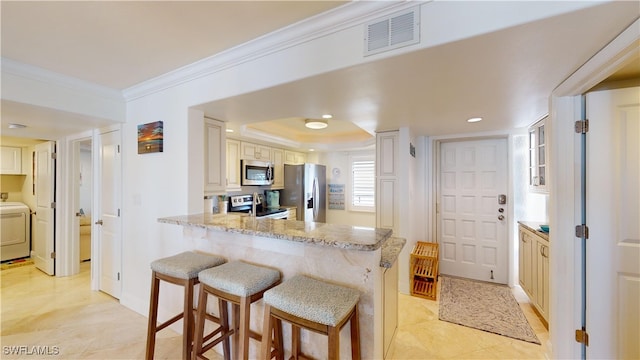 kitchen featuring stainless steel appliances, kitchen peninsula, light stone countertops, a kitchen bar, and washer / dryer