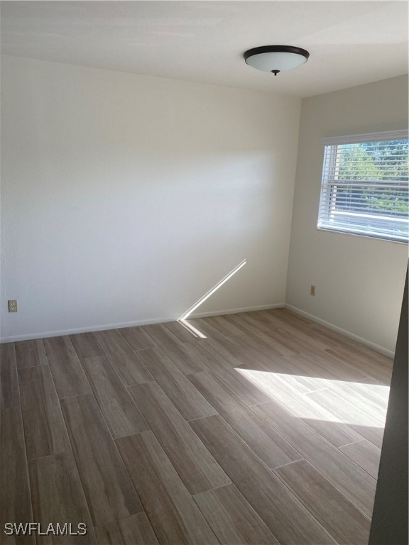 spare room with baseboards and wood finished floors