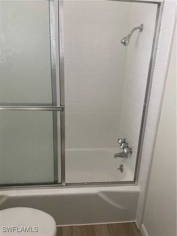 bathroom featuring combined bath / shower with glass door, wood finished floors, and toilet