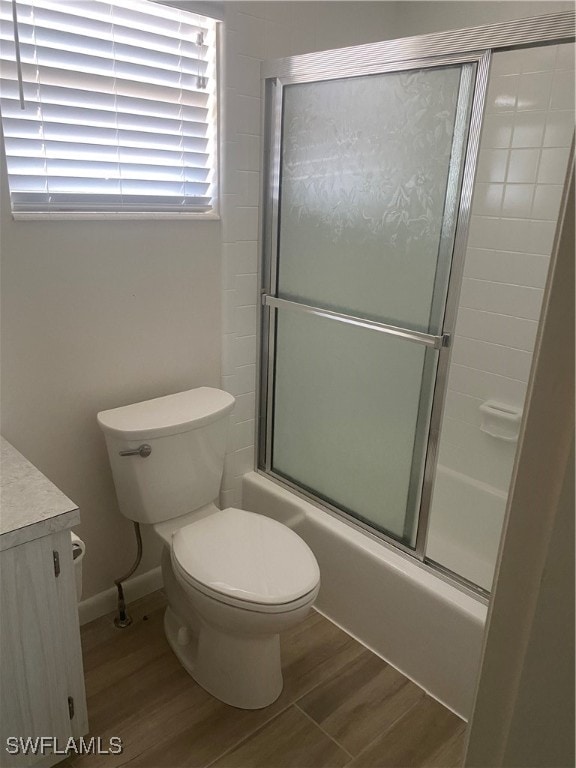 full bathroom with toilet, combined bath / shower with glass door, vanity, wood finished floors, and baseboards