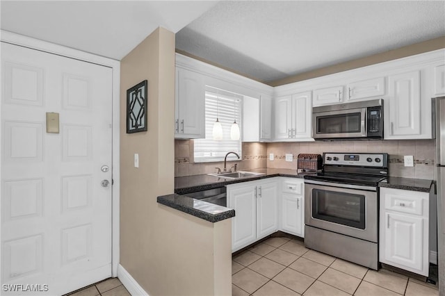 kitchen with appliances with stainless steel finishes, backsplash, sink, white cabinets, and light tile patterned flooring