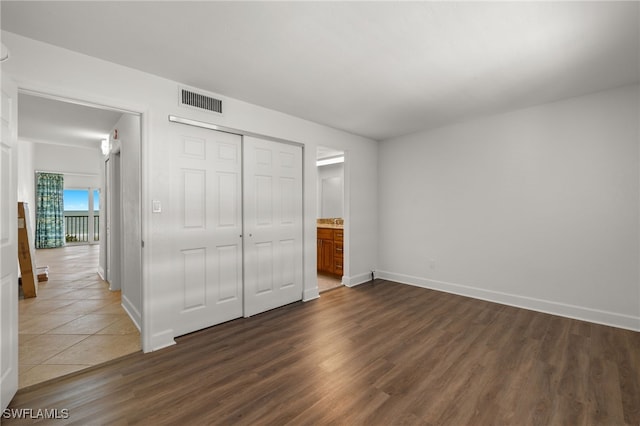 unfurnished bedroom with connected bathroom, a closet, and dark hardwood / wood-style flooring