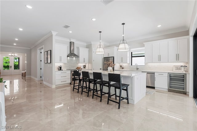 kitchen featuring stainless steel appliances, white cabinetry, beverage cooler, a kitchen island, and wall chimney range hood