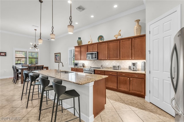 kitchen with light stone counters, stainless steel appliances, decorative light fixtures, sink, and a kitchen island with sink