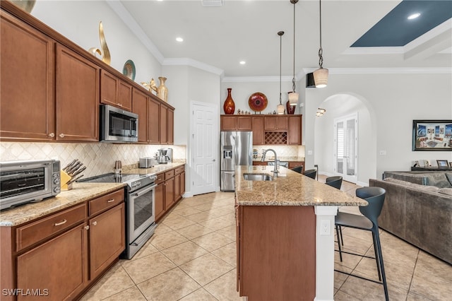 kitchen featuring stainless steel appliances, a center island with sink, sink, crown molding, and pendant lighting