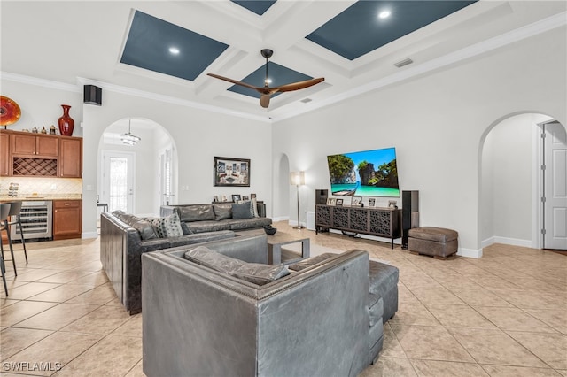 tiled living room featuring ornamental molding, a towering ceiling, wine cooler, coffered ceiling, and ceiling fan