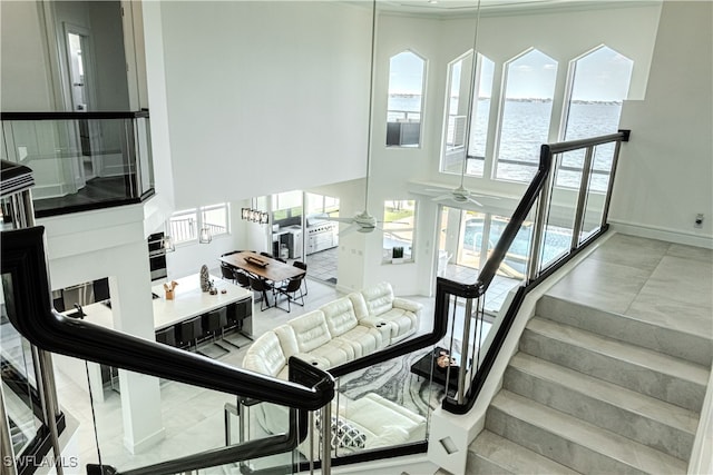 staircase with ceiling fan, a high ceiling, a water view, and baseboards