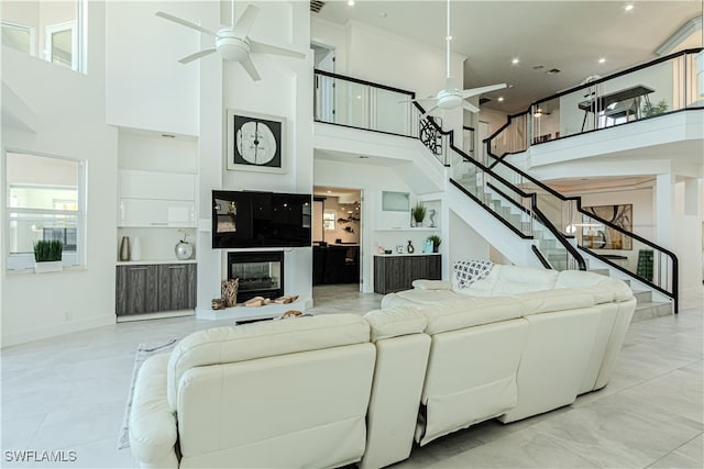 living room with a glass covered fireplace, ceiling fan, stairway, and a high ceiling