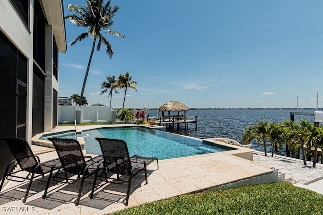 view of pool featuring a water view, an infinity pool, fence, and a patio