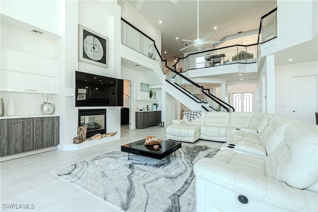 living room featuring visible vents, ceiling fan, stairway, a high ceiling, and a multi sided fireplace