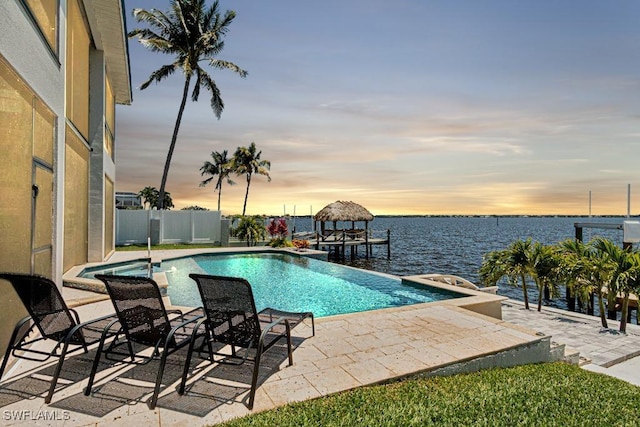 view of swimming pool featuring an infinity pool, a patio area, a water view, and fence