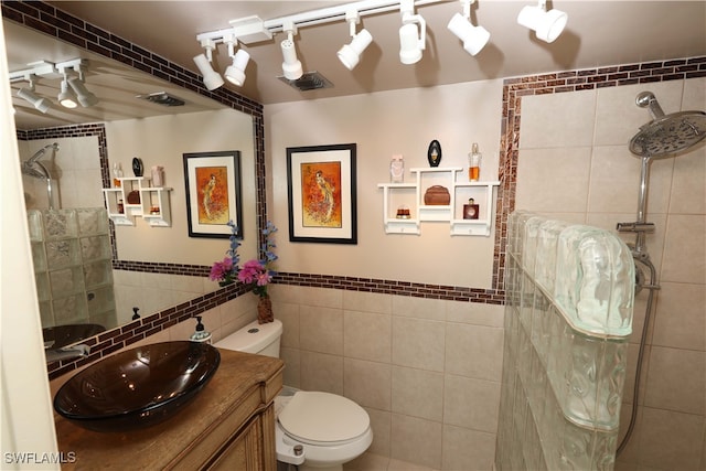 bathroom featuring tile walls, toilet, a tile shower, and vanity