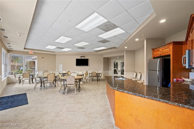 kitchen with appliances with stainless steel finishes, kitchen peninsula, sink, dark stone countertops, and light tile patterned flooring