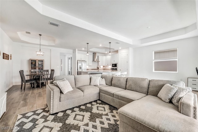 living room with a tray ceiling, an inviting chandelier, and light hardwood / wood-style flooring