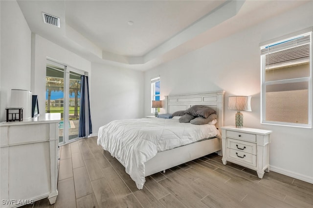 bedroom with a tray ceiling, light hardwood / wood-style floors, and access to outside