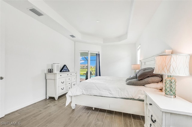 bedroom with light wood-type flooring, a raised ceiling, and access to exterior