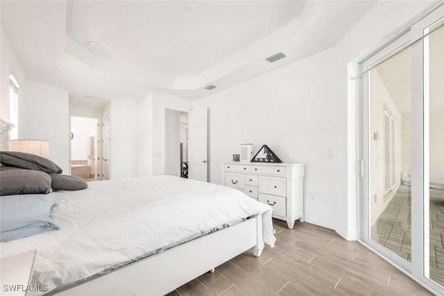 bedroom featuring light wood-type flooring, a raised ceiling, and ensuite bath