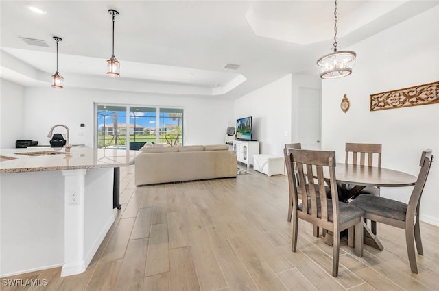 dining area with light hardwood / wood-style floors, a raised ceiling, and sink