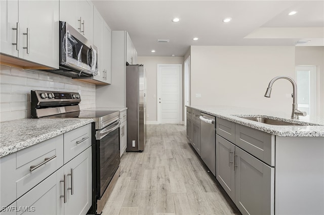 kitchen with light wood-type flooring, light stone counters, stainless steel appliances, and sink