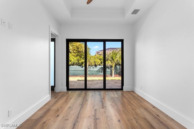 unfurnished room with a raised ceiling, ceiling fan, and light wood-type flooring