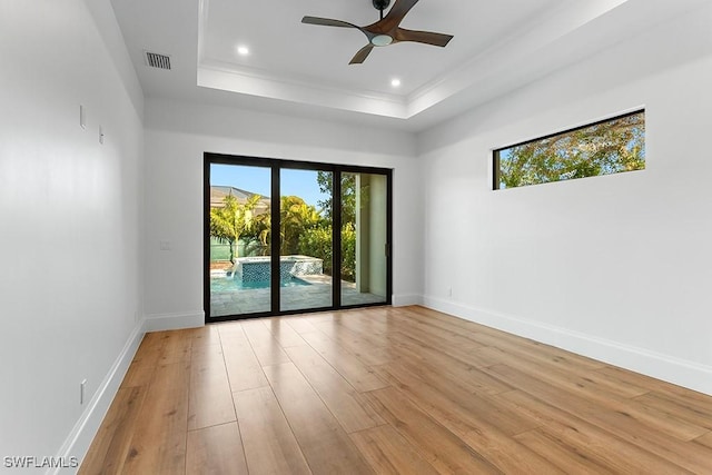 empty room with a raised ceiling, ceiling fan, and light wood-type flooring