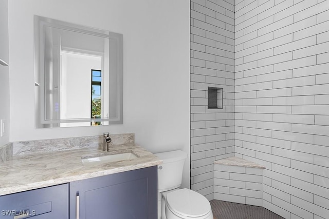 bathroom with tiled shower, vanity, and toilet