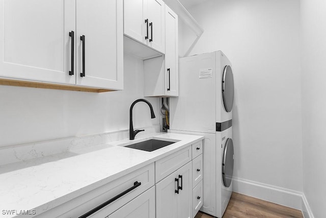 clothes washing area featuring cabinets, sink, stacked washing maching and dryer, and light wood-type flooring