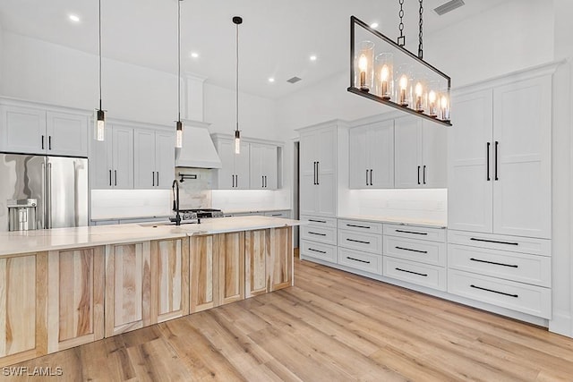 kitchen with backsplash, white cabinets, a center island with sink, decorative light fixtures, and high end fridge