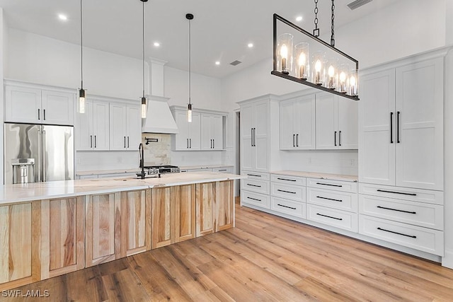 kitchen featuring decorative light fixtures, decorative backsplash, high end fridge, white cabinets, and custom range hood