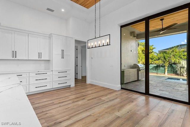 unfurnished dining area with ceiling fan, light hardwood / wood-style flooring, wooden ceiling, and a high ceiling