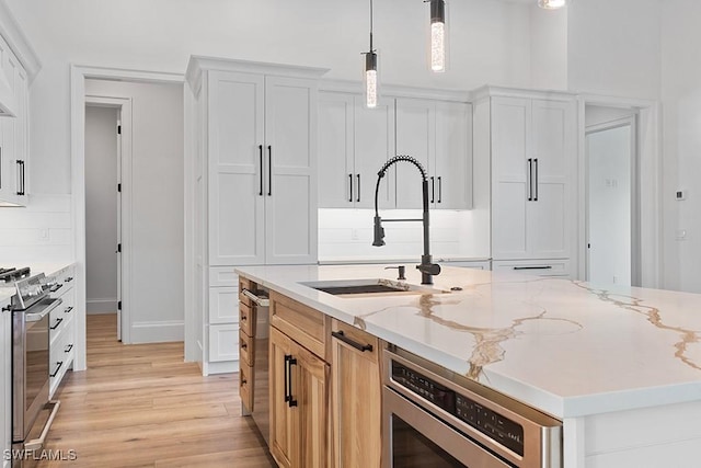 kitchen with pendant lighting, stainless steel gas stove, light stone counters, and white cabinetry