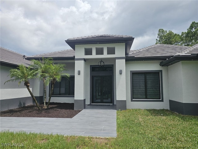 doorway to property featuring a yard, a tile roof, and stucco siding