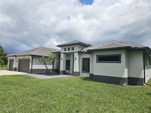 prairie-style house featuring an attached garage, stucco siding, a tile roof, and a front yard