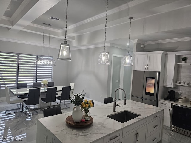 kitchen with hanging light fixtures, white cabinetry, sink, stainless steel fridge, and a kitchen island with sink