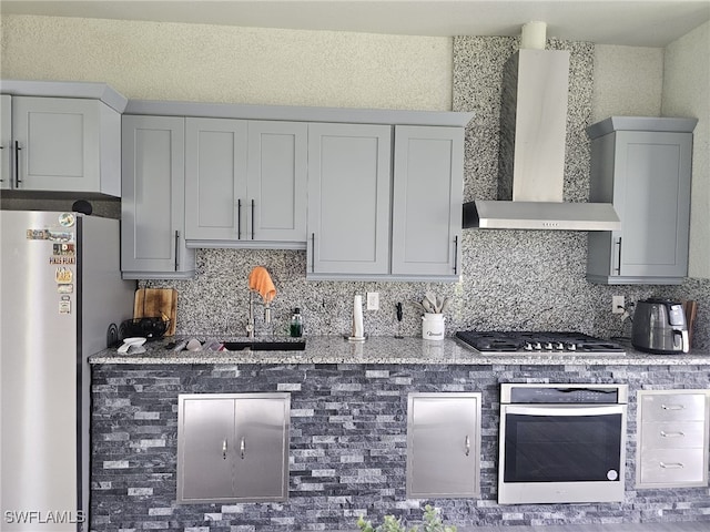 kitchen with backsplash, stainless steel appliances, wall chimney exhaust hood, and light stone countertops