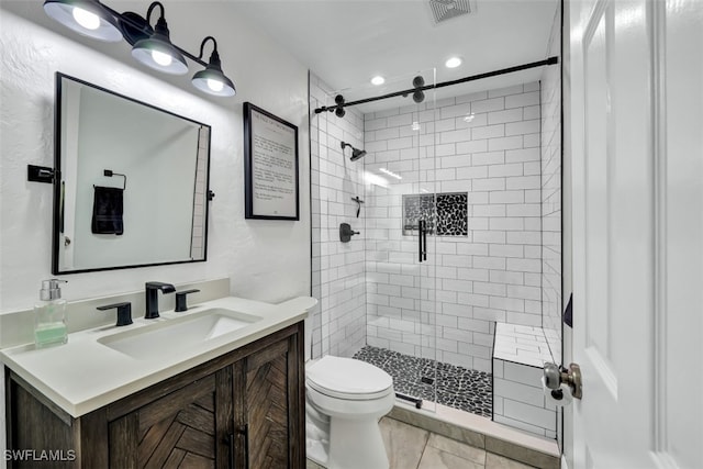 bathroom with vanity, toilet, a tile shower, and tile patterned flooring