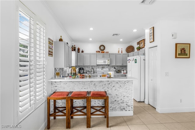 kitchen featuring white appliances, light tile patterned floors, a breakfast bar, kitchen peninsula, and ornamental molding