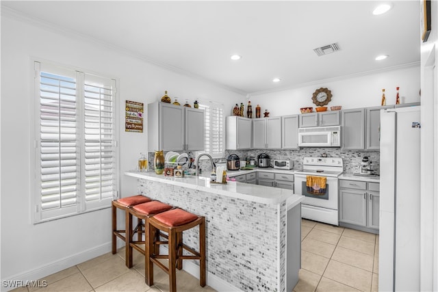 kitchen featuring backsplash, light tile patterned floors, white appliances, kitchen peninsula, and a breakfast bar