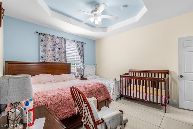 bedroom with a raised ceiling, light tile patterned floors, and ceiling fan