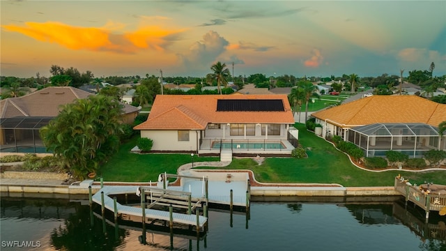 back house at dusk featuring a patio, a water view, glass enclosure, and a lawn